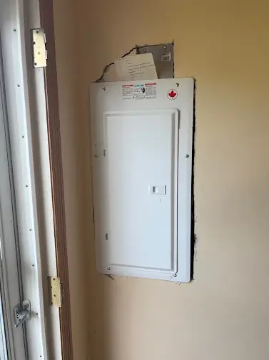 New white panel cover mounted in a wall with the drywall cut back around it and the panel schedule paperwork tucked in the top