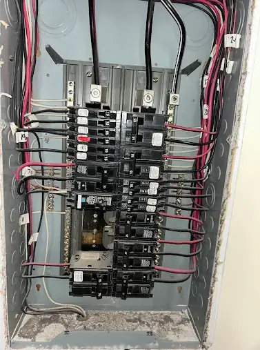 Open breaker panel with two columns of breakers, red and black conductors and a dusty enclosure