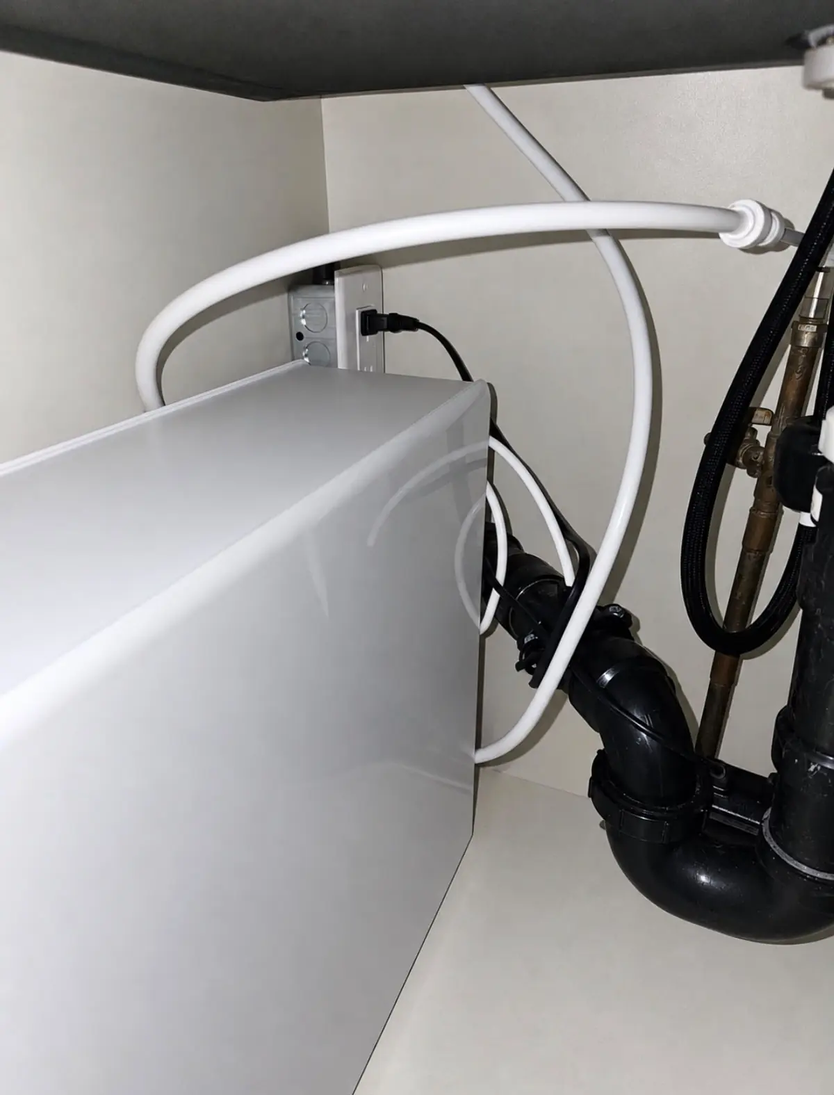 Outlet installed under a kitchen sink powering a water filtration unit, with the plumbing beside it