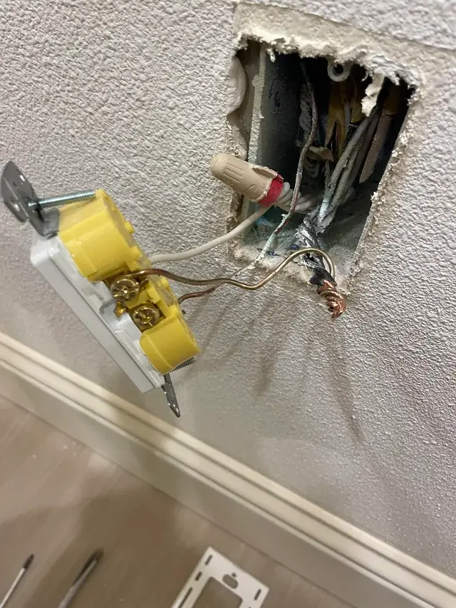 Old yellow receptacle pulled out of a wall box showing marrette splices and bare copper inside the box